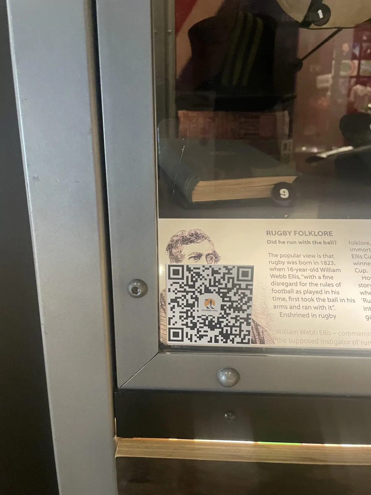 A Journey Pal QR code printed on an exhibit label inside a display case at the New Zealand Rugby Museum
